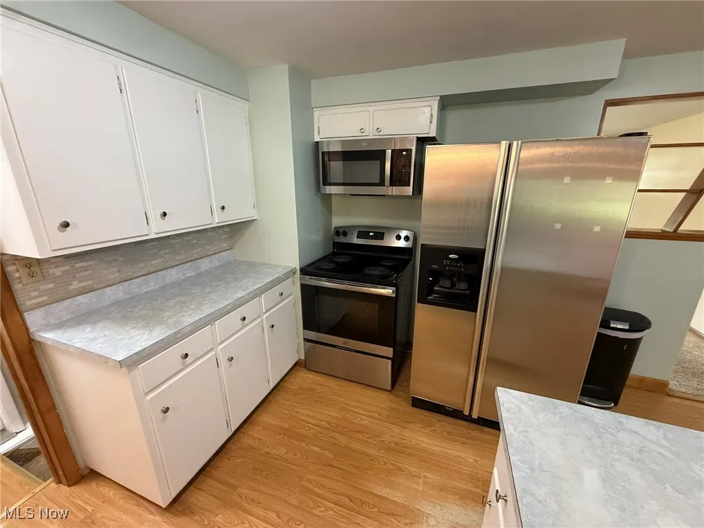 Kitchen with appliances with stainless steel finishes, white cabinets, light wood-style flooring, light countertops, and tasteful backsplash