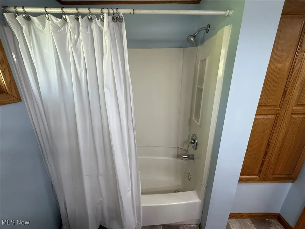 Full bathroom with shower / tub combo with curtain and baseboards