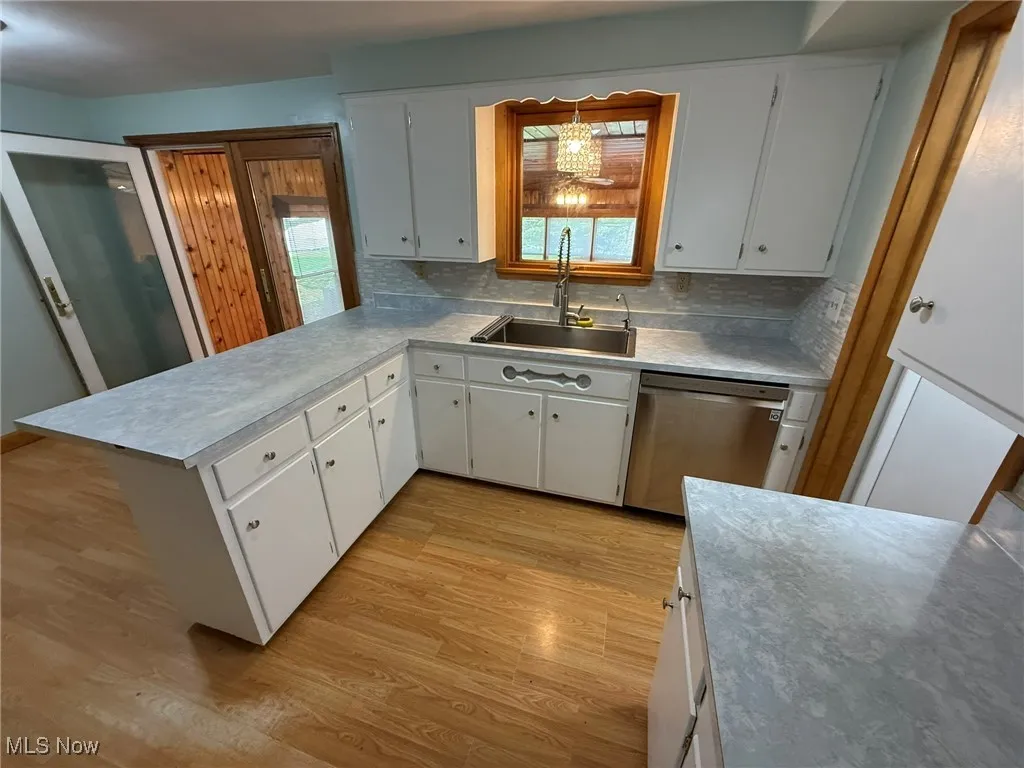 Kitchen with white cabinetry, dishwasher, light wood-style flooring, tasteful backsplash, and light countertops