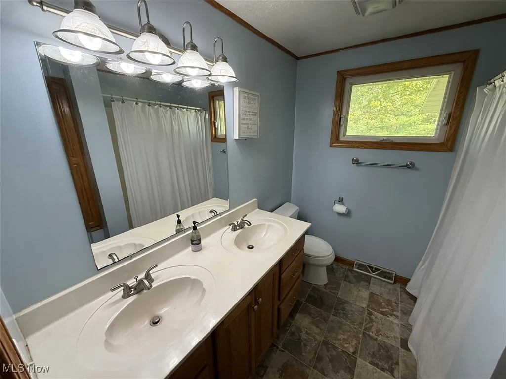Full bath featuring stone finish flooring, double vanity, a shower with curtain, and crown molding