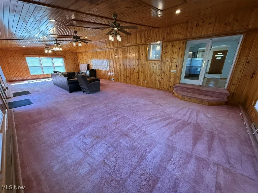 Carpeted living room featuring wooden walls, wood ceiling, and a ceiling fan