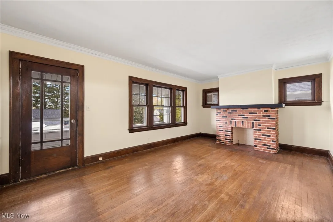 Unfurnished living room with dark wood-style flooring, ornamental molding, healthy amount of natural light, and a fireplace