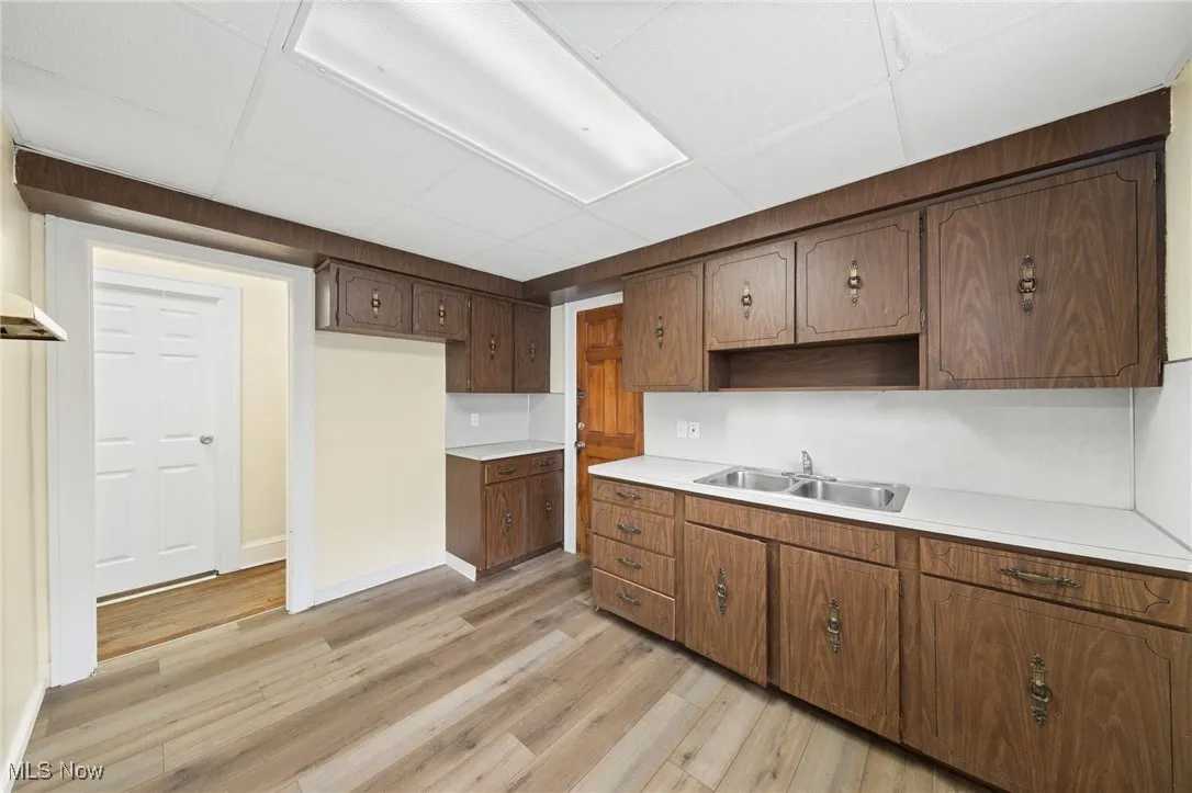 Kitchen with light countertops, a paneled ceiling, light wood-type flooring, open shelves, and dark brown cabinetry