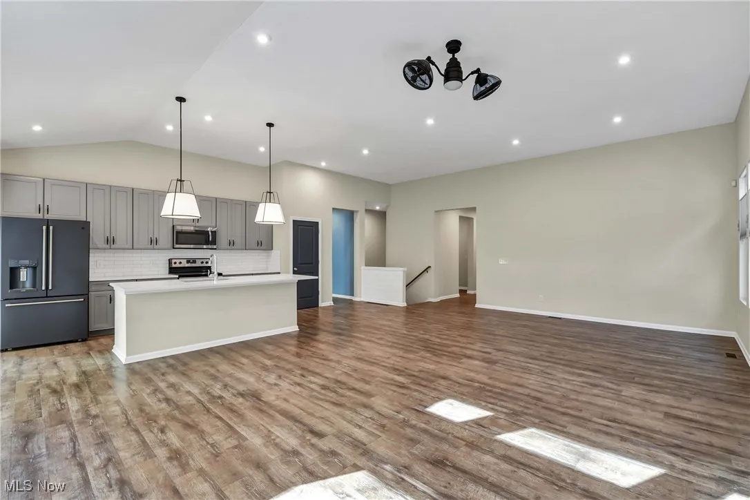 Kitchen with gray cabinets, appliances with stainless steel finishes, open floor plan, pendant lighting, and a center island with sink