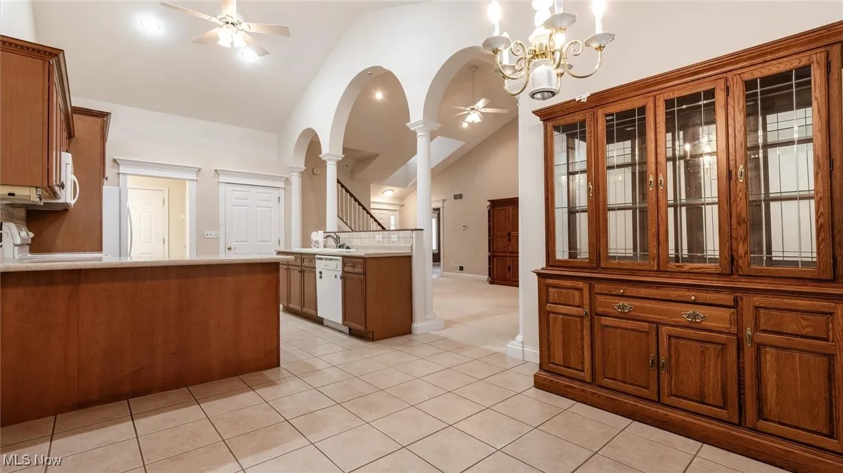 Kitchen with brown cabinets, ceiling fan, light tile patterned floors, white appliances, and high vaulted ceiling