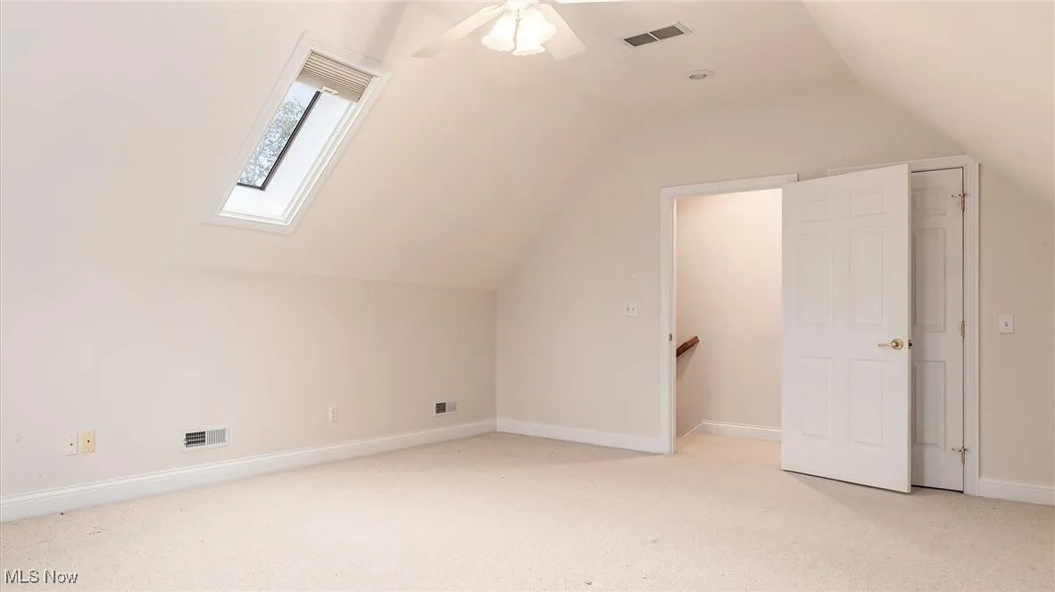 Bonus room with light colored carpet, a skylight, vaulted ceiling, and ceiling fan
