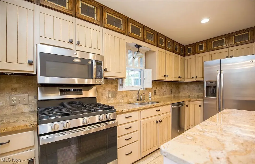 Kitchen with stainless steel appliances, decorative backsplash, glass insert cabinets, light stone countertops, and recessed lighting