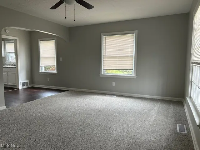 Unfurnished room featuring dark carpet, a ceiling fan, and arched walkways