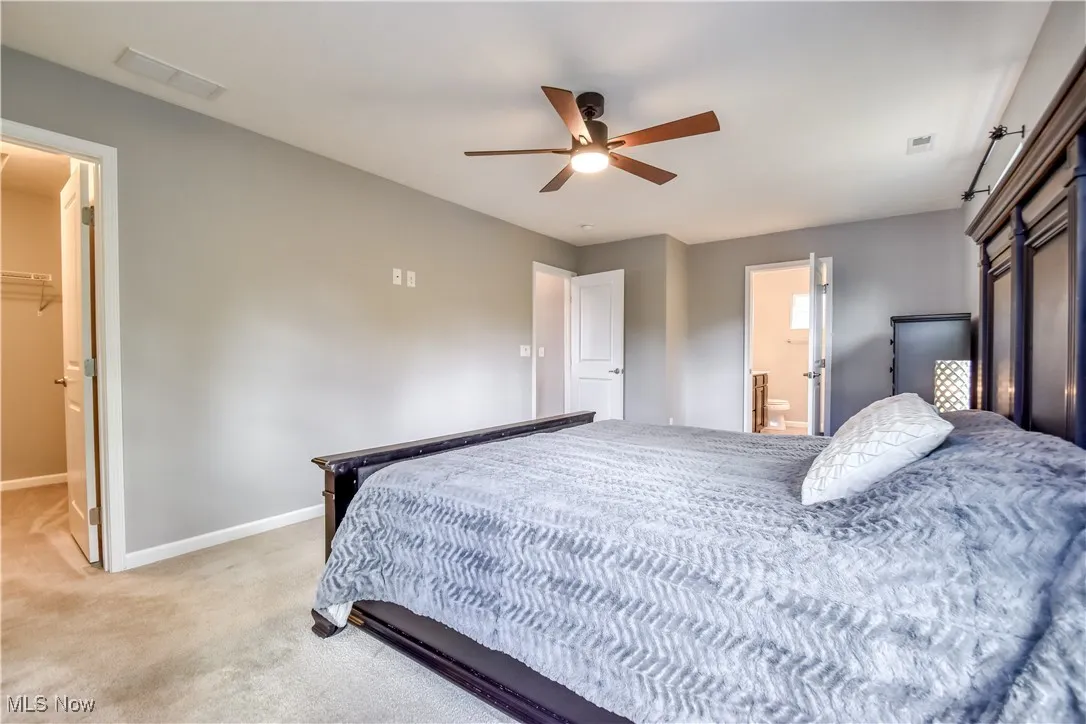 Carpeted bedroom featuring a walk in closet, ceiling fan, and ensuite bath