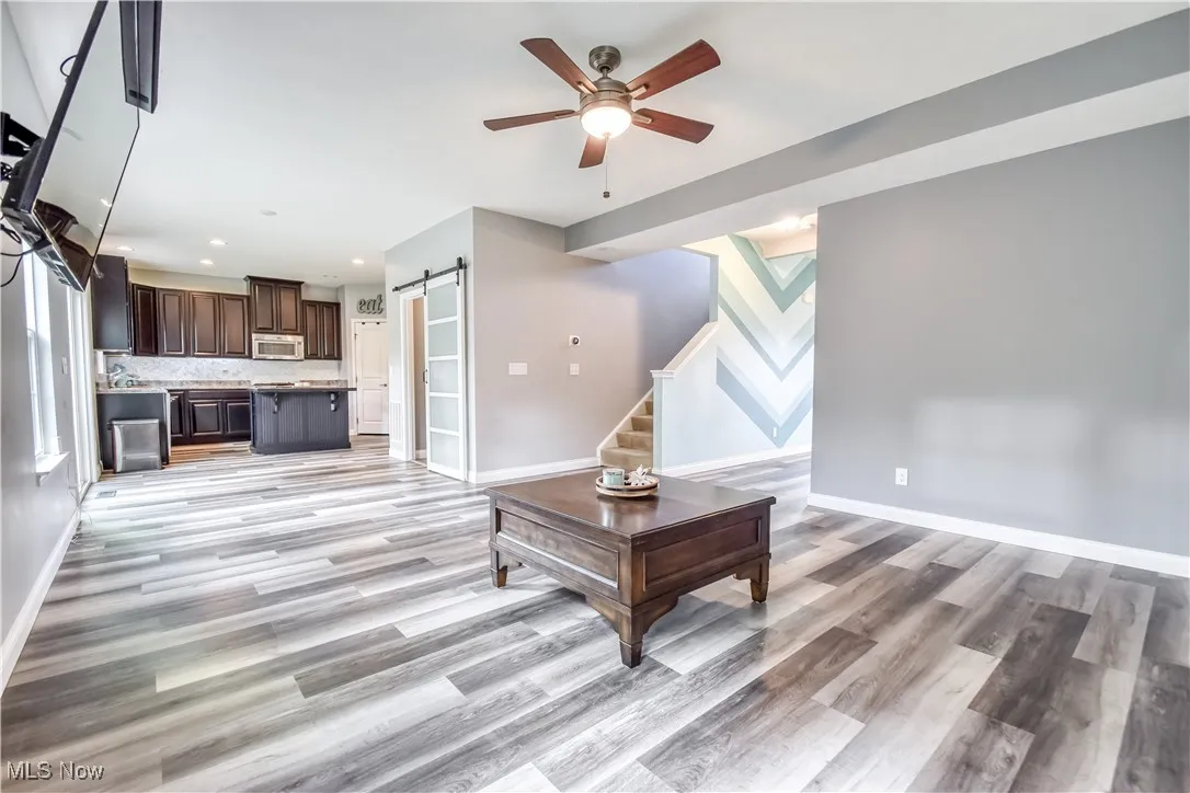 Living area with a barn door, stairs, ceiling fan, recessed lighting, and light wood-type flooring