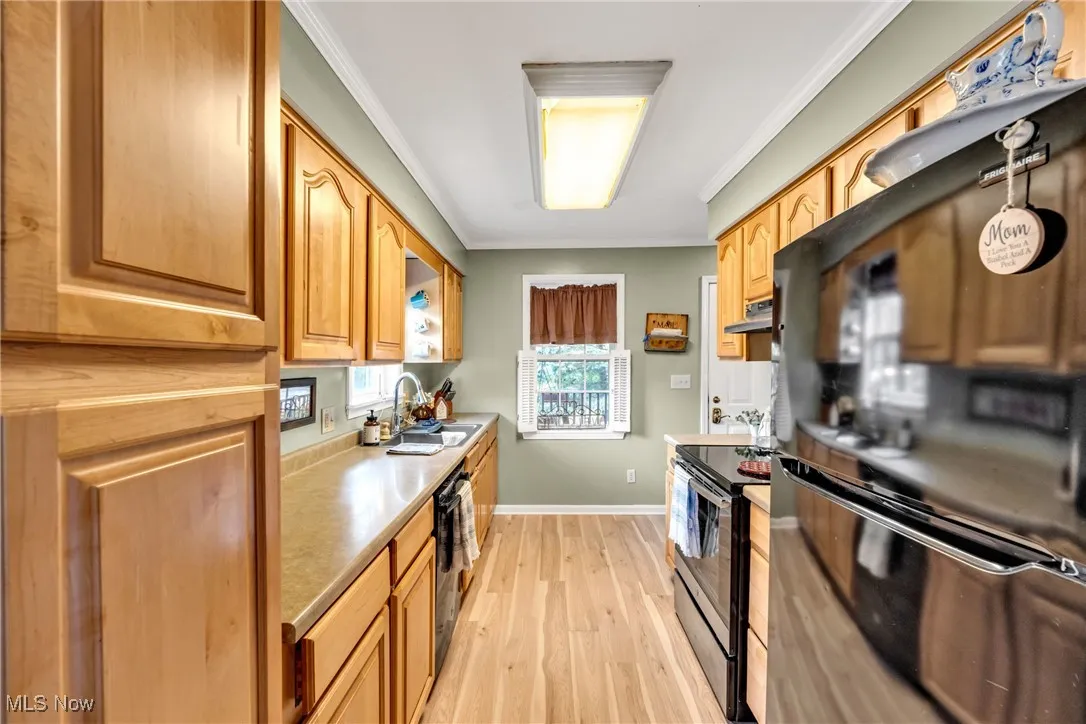 Kitchen featuring black appliances, ornamental molding, light wood finished floors, light countertops, and under cabinet range hood