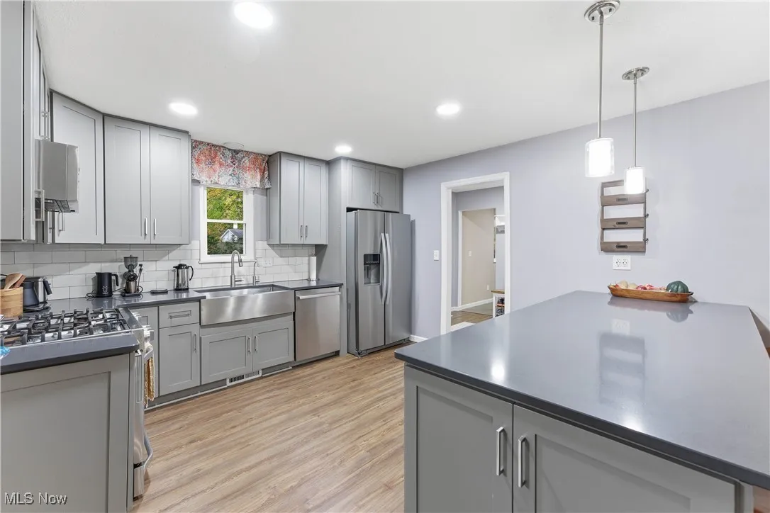 Kitchen featuring gray cabinets, appliances with stainless steel finishes, tasteful backsplash, pendant lighting, and light wood-style flooring