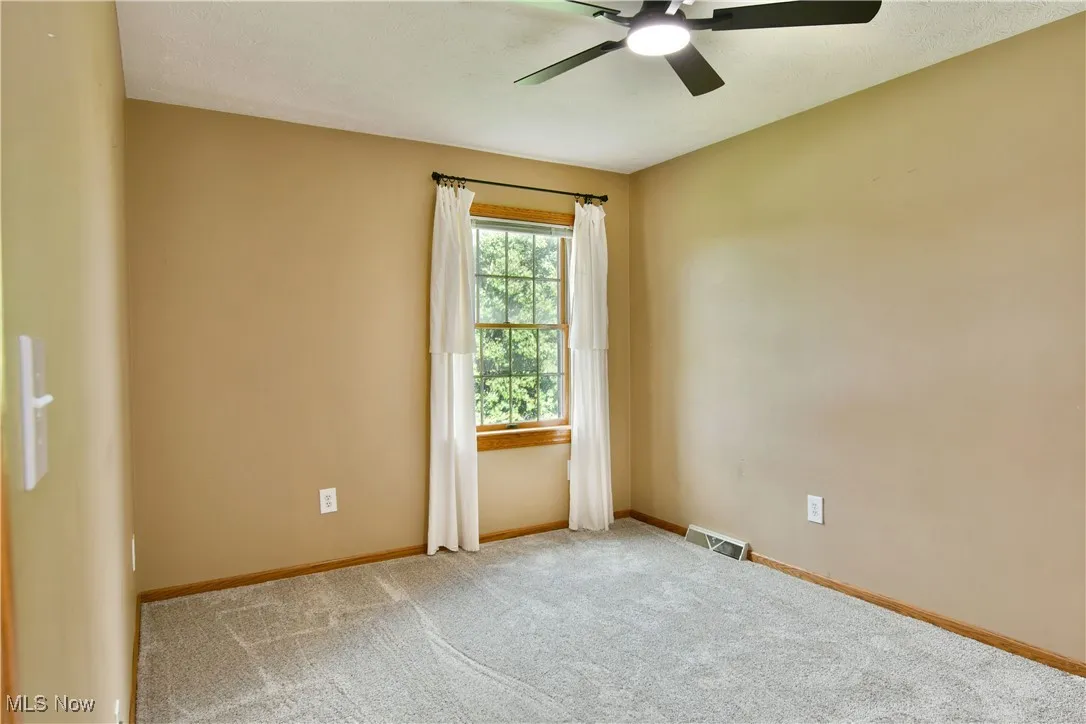 Carpeted spare room featuring ceiling fan and baseboards
