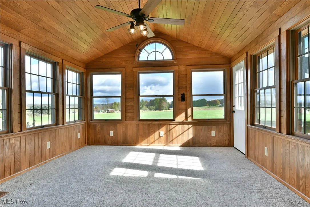 Unfurnished sunroom with wooden walls, wooden ceiling, vaulted ceiling, and carpet floors
