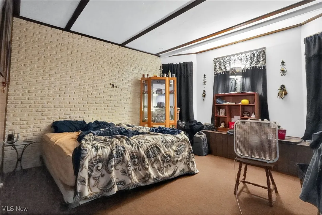 Bedroom with brick wall, beamed ceiling, and light carpet