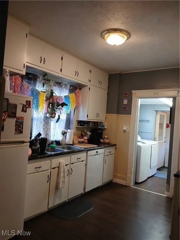 Kitchen featuring fridge, dark countertops, a textured ceiling, dark wood-type flooring, and washing machine and clothes dryer