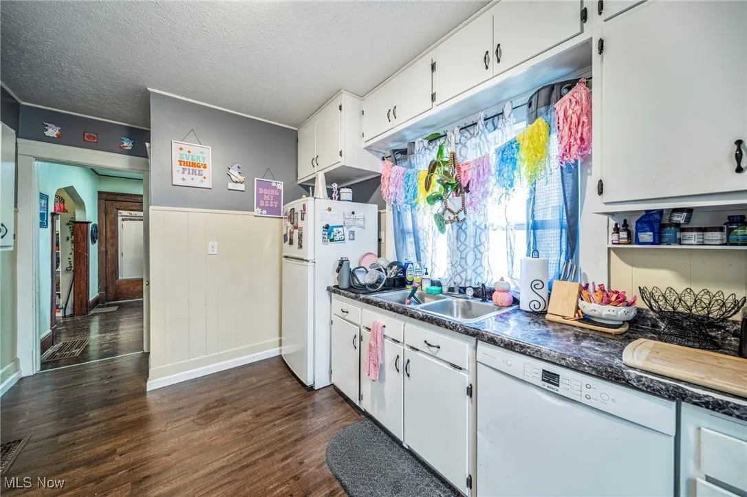 Kitchen with white appliances, dark wood finished floors, a textured ceiling, white cabinets, and dark countertops.