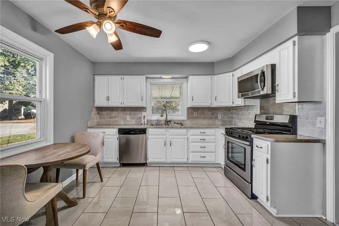 Kitchen with tasteful backsplash, stainless steel appliances, white cabinetry, and light countertops