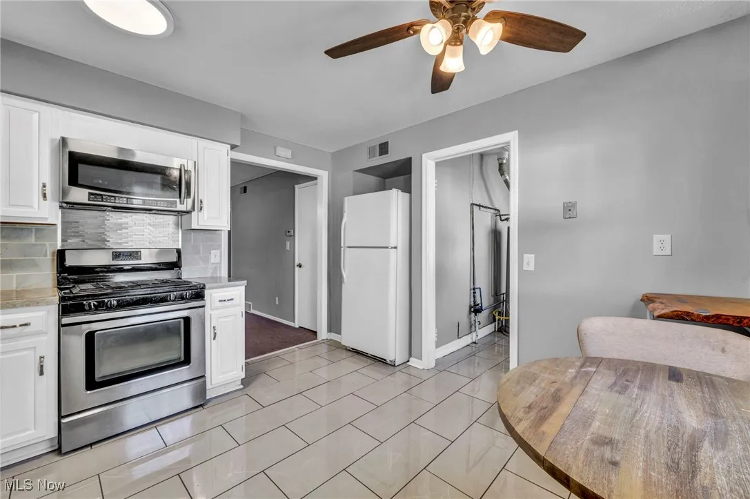 Kitchen with appliances with stainless steel finishes, white cabinetry, backsplash, and a ceiling fan