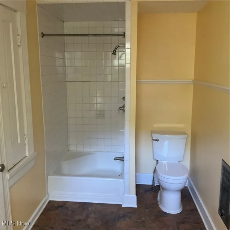 Yellow bedroom has adjacent Full bath featuring bathtub / shower combination and dark tile patterned floors