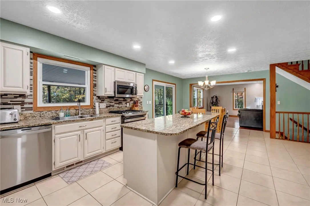 Kitchen with light stone counters, a kitchen island, a textured ceiling, appliances with stainless steel finishes, and white cabinets