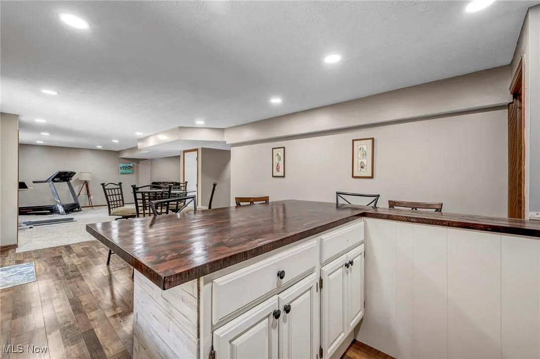 Kitchen featuring recessed lighting, white cabinets, butcher block countertops, dark wood-type flooring, and a kitchen bar