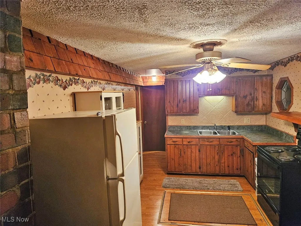Kitchen with black electric range oven, dark countertops, freestanding refrigerator, a textured ceiling, and light wood finished floors