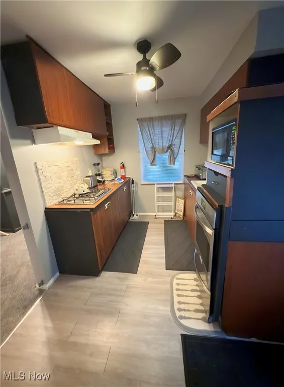 Kitchen featuring a ceiling fan, under cabinet range hood, stainless steel appliances, light wood finished floors, and brown cabinetry