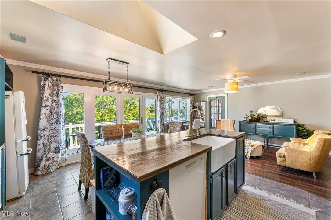 Kitchen with ornamental molding, white appliances, decorative light fixtures, wooden counters, and an island with sink