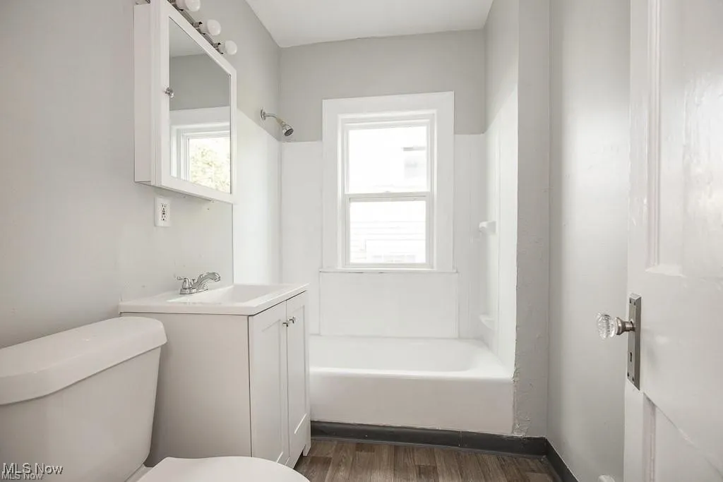 Full bathroom with healthy amount of natural light, dark wood finished floors, vanity, and washtub / shower combination
