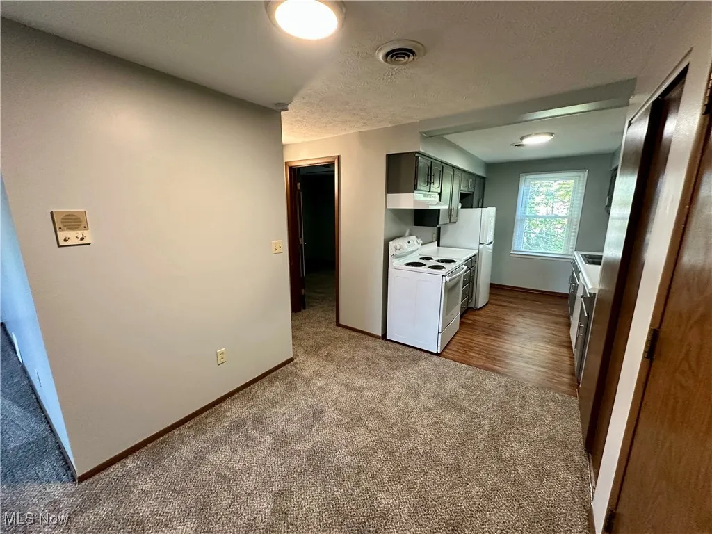 Kitchen with dark carpet, white electric range, a textured ceiling, light countertops, and under cabinet range hood