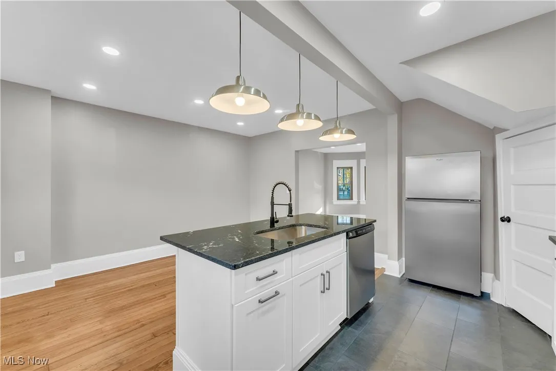 Kitchen featuring appliances with stainless steel finishes, dark stone counters, white cabinets, decorative light fixtures, and a kitchen island with sink