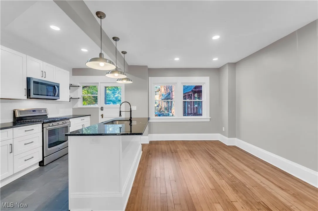 Kitchen featuring stainless steel appliances, open shelves, decorative light fixtures, dark stone countertops, and white cabinetry