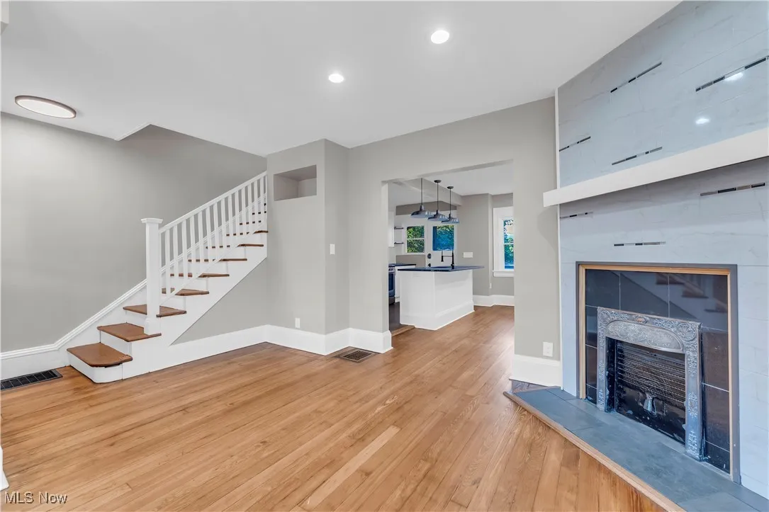 Unfurnished living room with a tile fireplace, light wood finished floors, stairs, and recessed lighting