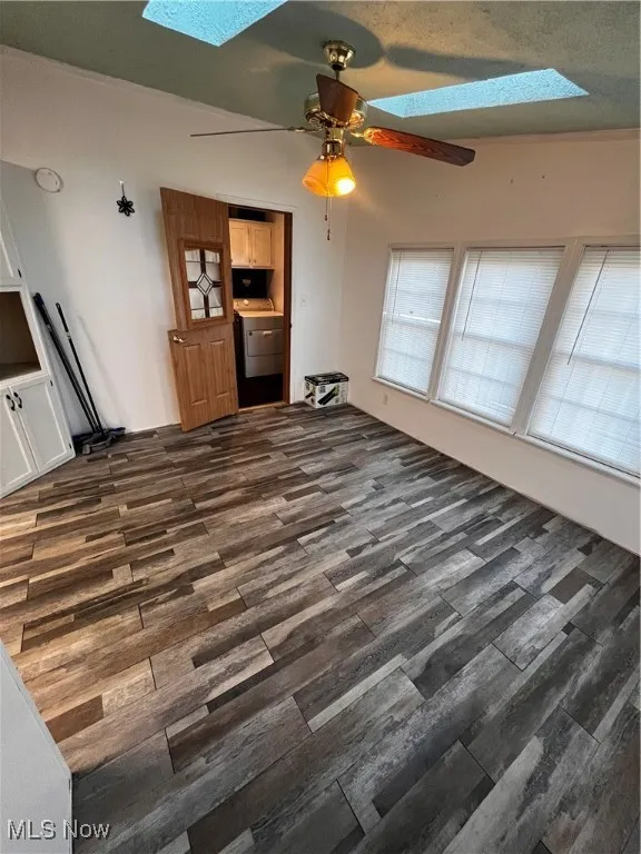 Unfurnished living room with a skylight, washer / clothes dryer, dark wood-type flooring, a textured ceiling, and ceiling fan