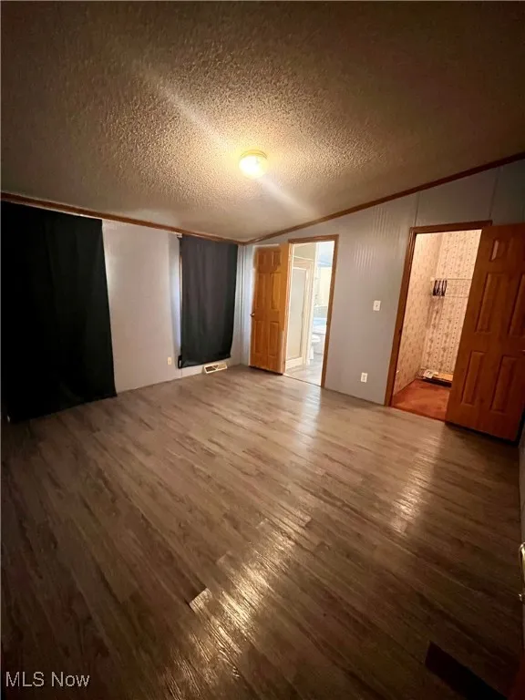 Unfurnished bedroom featuring crown molding, dark wood-style flooring, and a textured ceiling