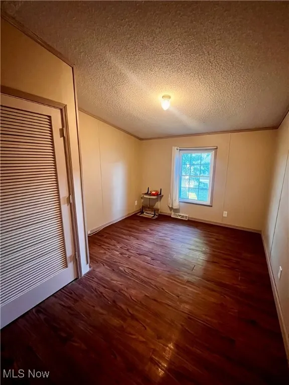 Spare room featuring ornamental molding, dark wood-style flooring, a textured ceiling, and a decorative wall
