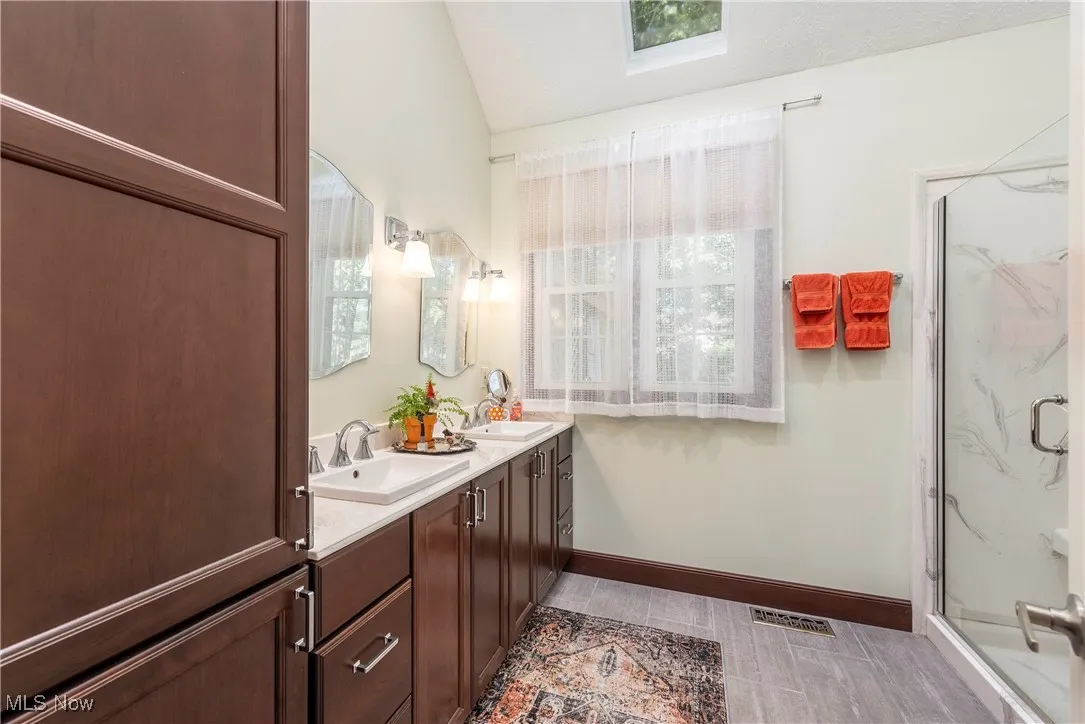 Full bath featuring double vanity, lofted ceiling, a marble finish shower, a skylight, and wood finish floors