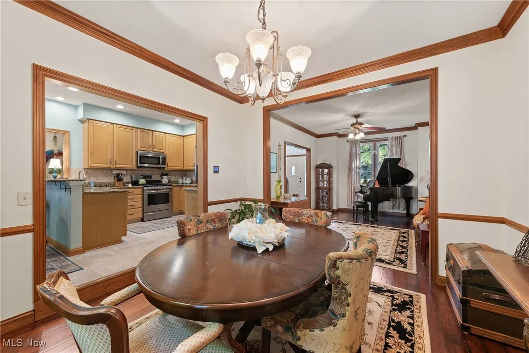 Dining space featuring crown molding, a ceiling fan, dark wood-type flooring, and a chandelier