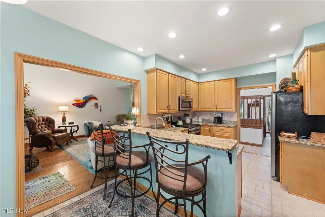 Kitchen featuring light stone countertops, decorative backsplash, stainless steel appliances, a kitchen breakfast bar, and recessed lighting