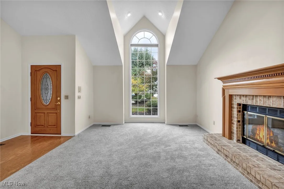 Unfurnished living room with carpet, a brick fireplace, and vaulted ceiling