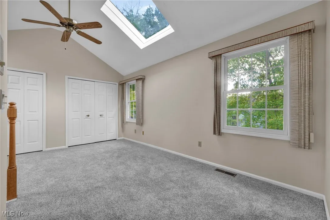 Unfurnished bedroom featuring high vaulted ceiling, two closets, carpet flooring, ceiling fan, and a skylight