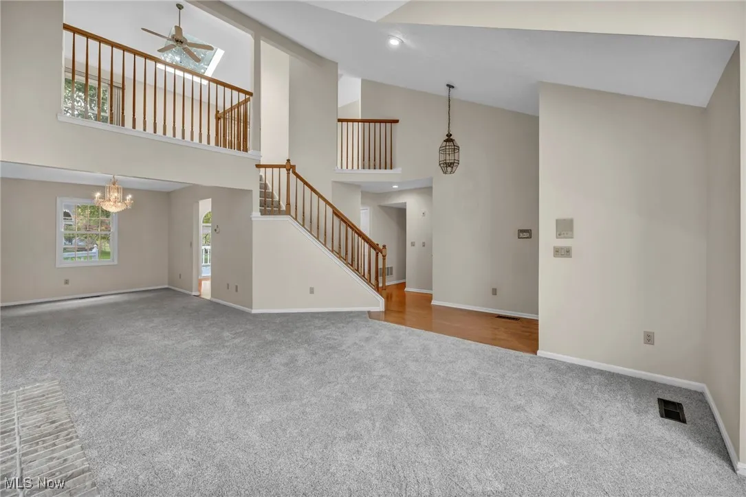 Unfurnished living room featuring carpet flooring, stairway, high vaulted ceiling, a chandelier, and a ceiling fan