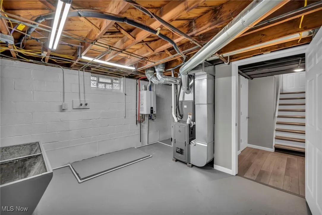 Basement featuring heating unit, stairs, and tankless water heater