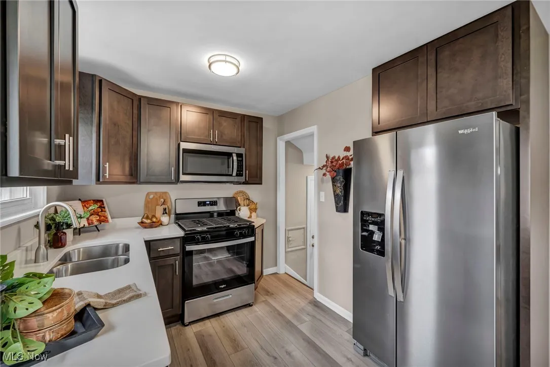 Kitchen with stainless steel appliances, dark brown cabinets, light wood finished floors, and light stone counters