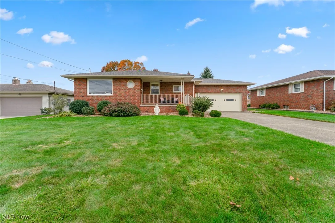 Single story home with covered porch, brick siding, a front yard, driveway, and a garage