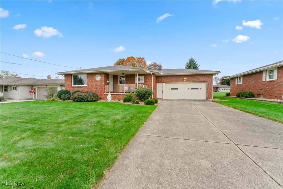 Ranch-style home featuring covered porch, a front yard, brick siding, and a garage