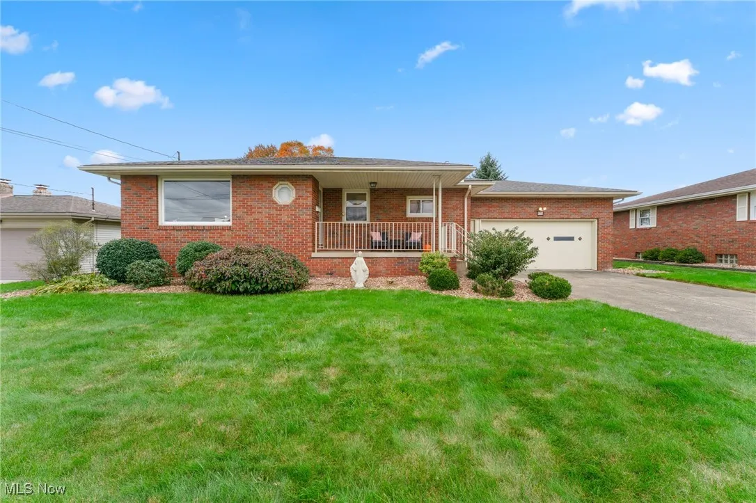 Ranch-style home with covered porch, brick siding, a front lawn, driveway, and a garage