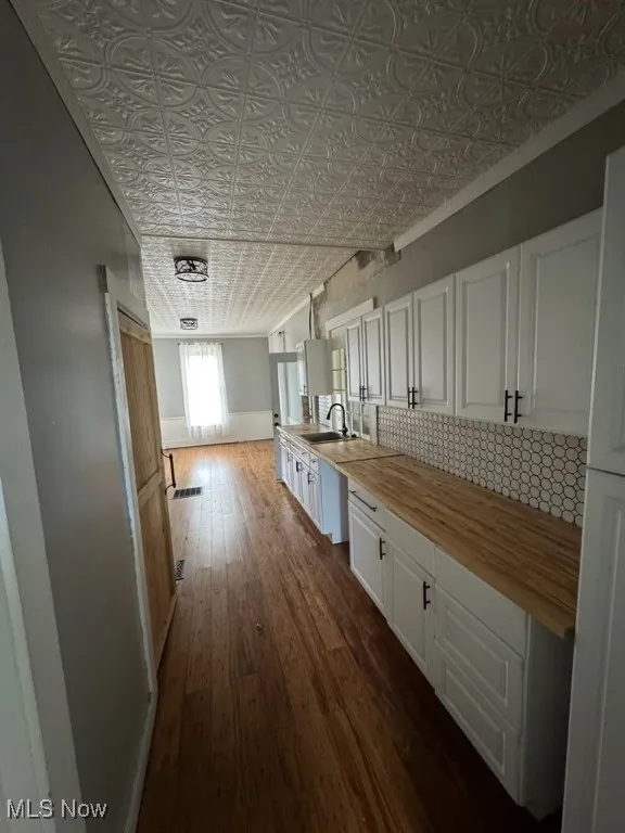 Kitchen with dark wood-type flooring, white cabinetry, an ornate ceiling, backsplash, and wood counters