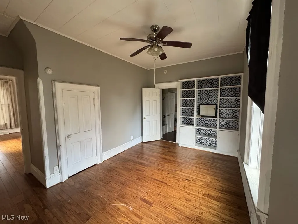 Unfurnished living room featuring wood finished floors, crown molding, and ceiling fan